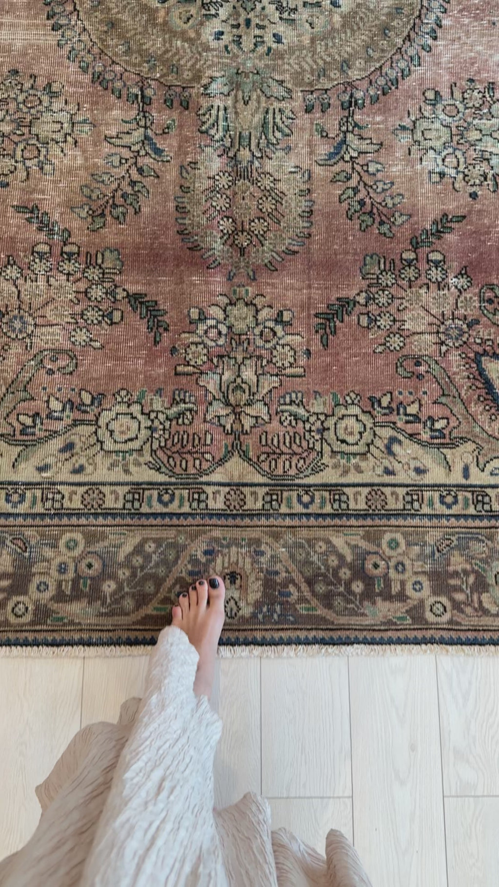 Woman standing on hand-knotted antique Persian 6x9 faded peach pink neutral area rug, highlighting texture and vintage floral detailing.