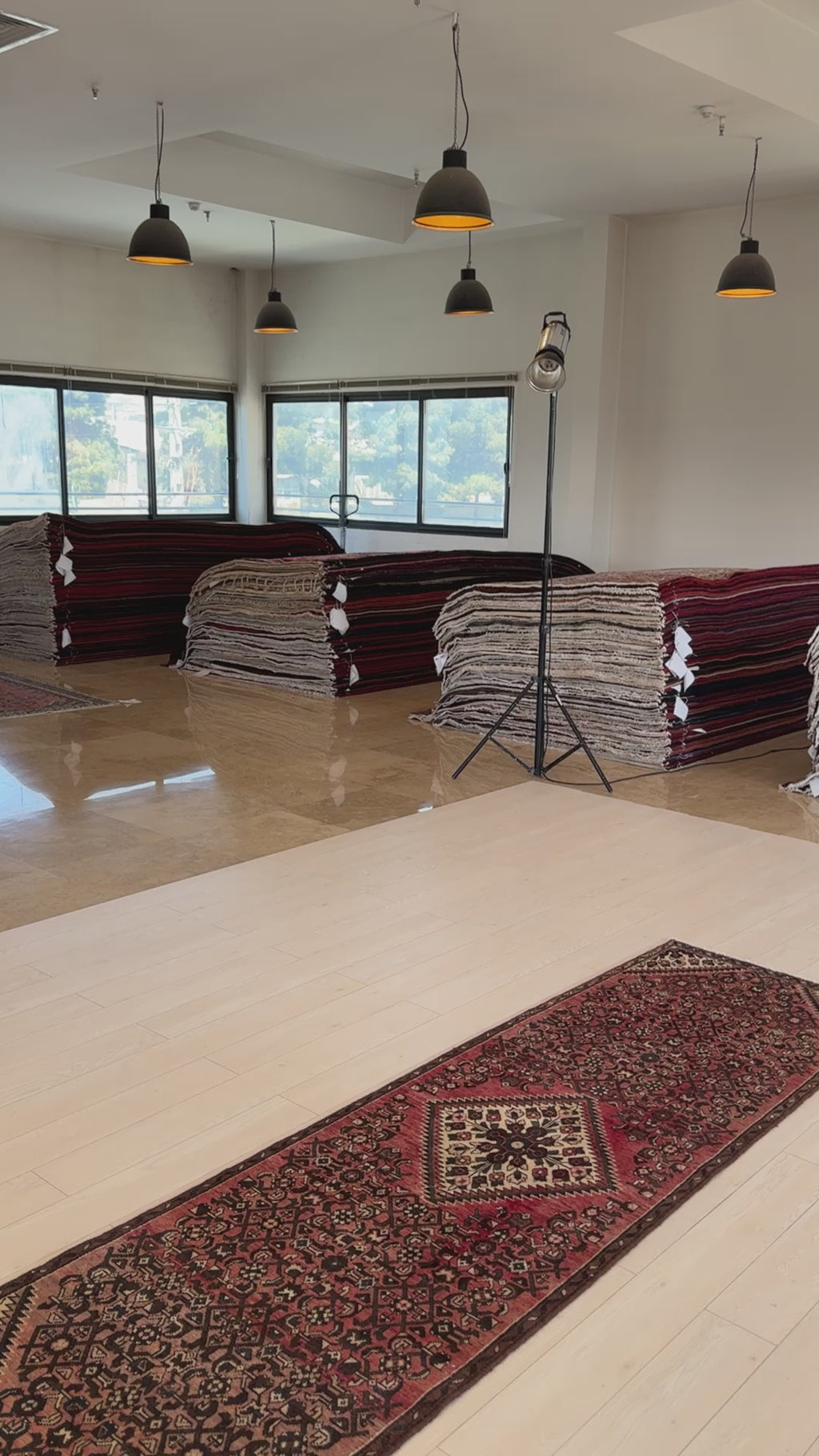 Close-up of the vintage wool runner rug in a showroom with stacked rugs in the background, highlighting its rich red and brown hues.