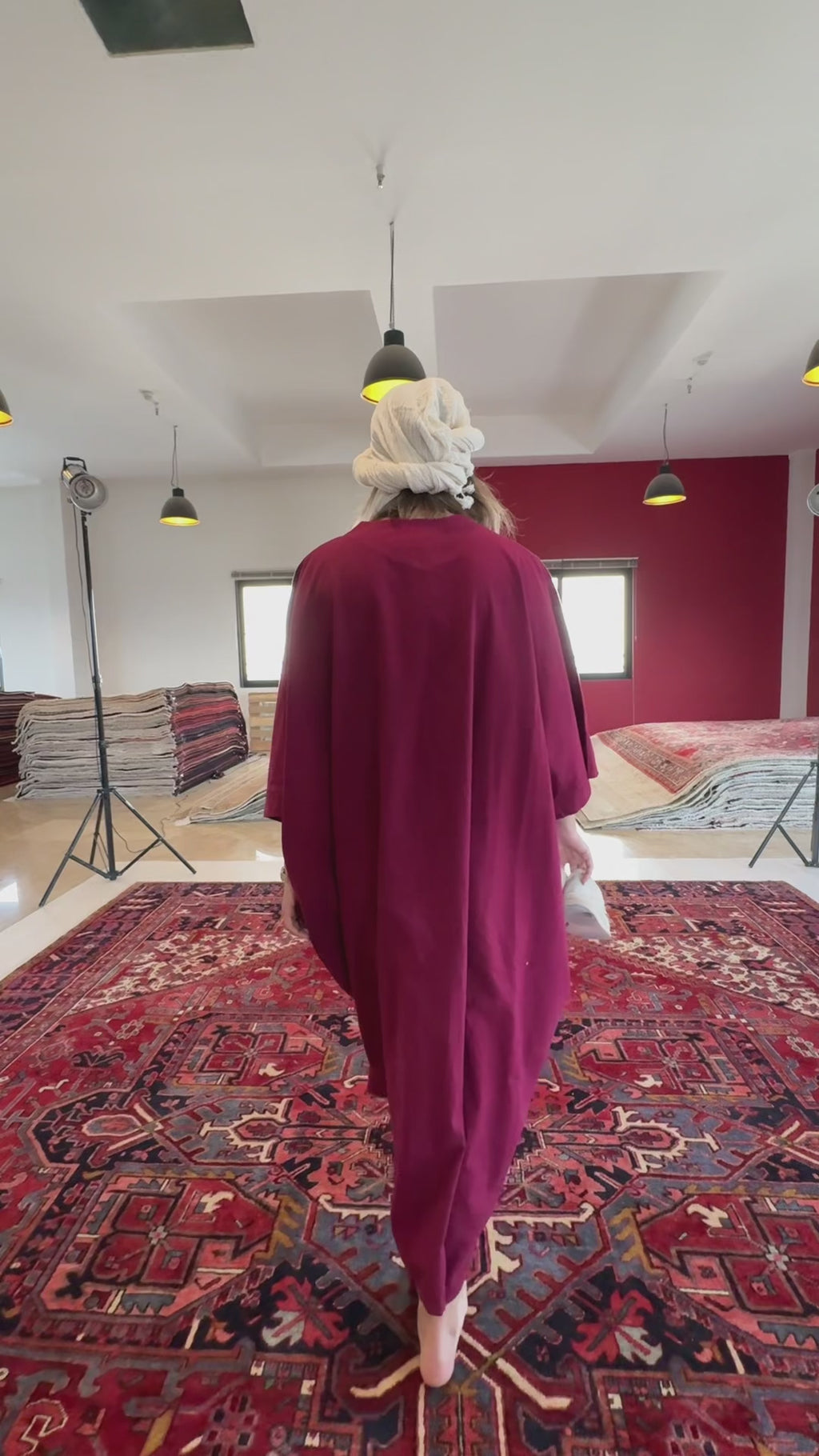 Back view of woman walking on Hand-Knotted Antique Red Persian Large Heriz Area Rug 11x13 in showroom with stacked rugs in background.