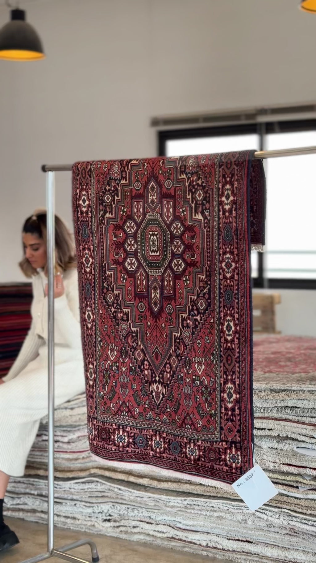 Hand-Knotted Vintage Wool Area Rug – 4' 7" x 2' 8" hanging on display rack in natural light, highlighting its detailed vintage motifs and deep colors.