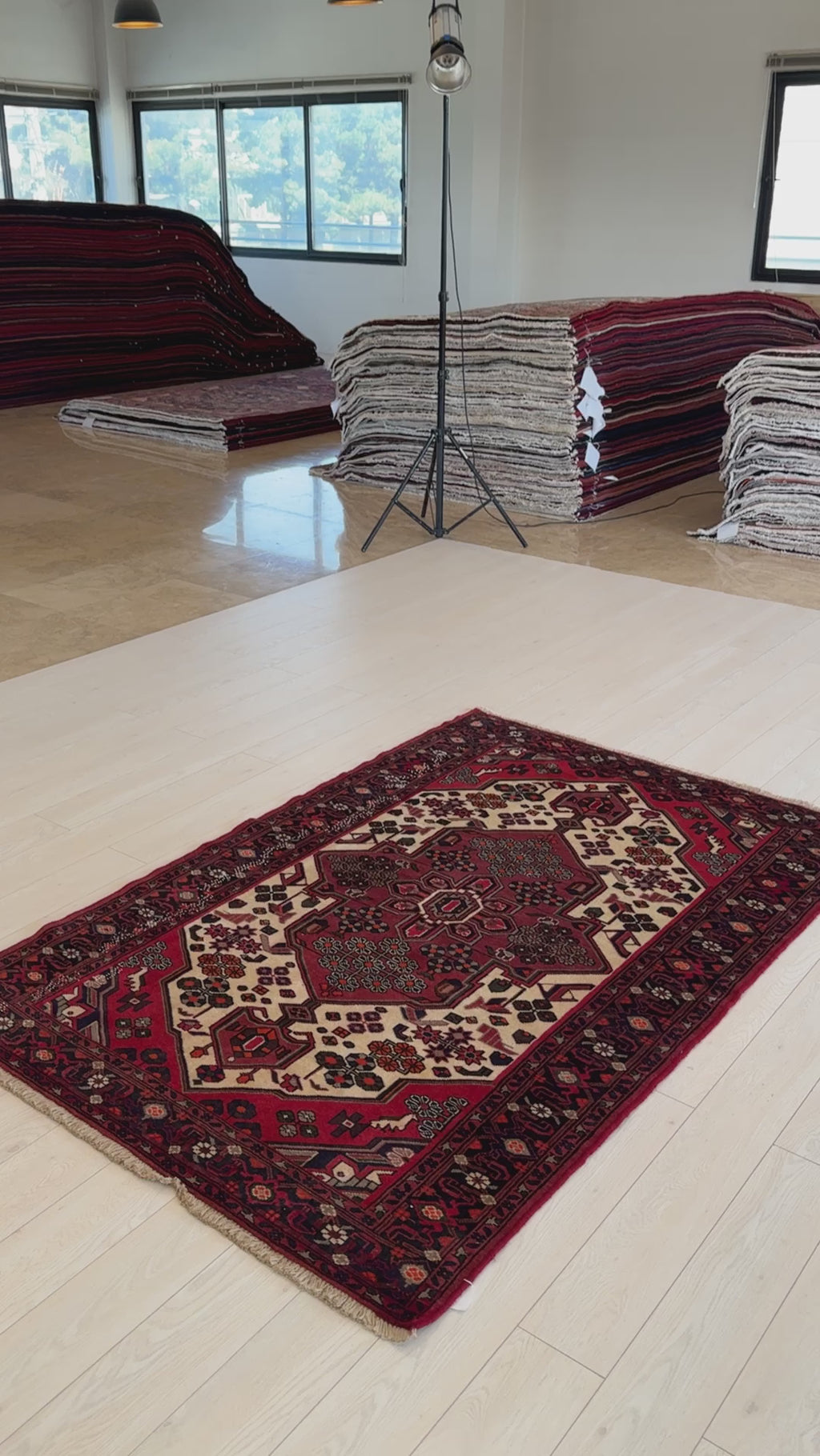 Hand-knotted vintage wool rug 6'7" x 4'4" displayed in a showroom with stacked rugs, showcasing its bold red and ivory geometric design.