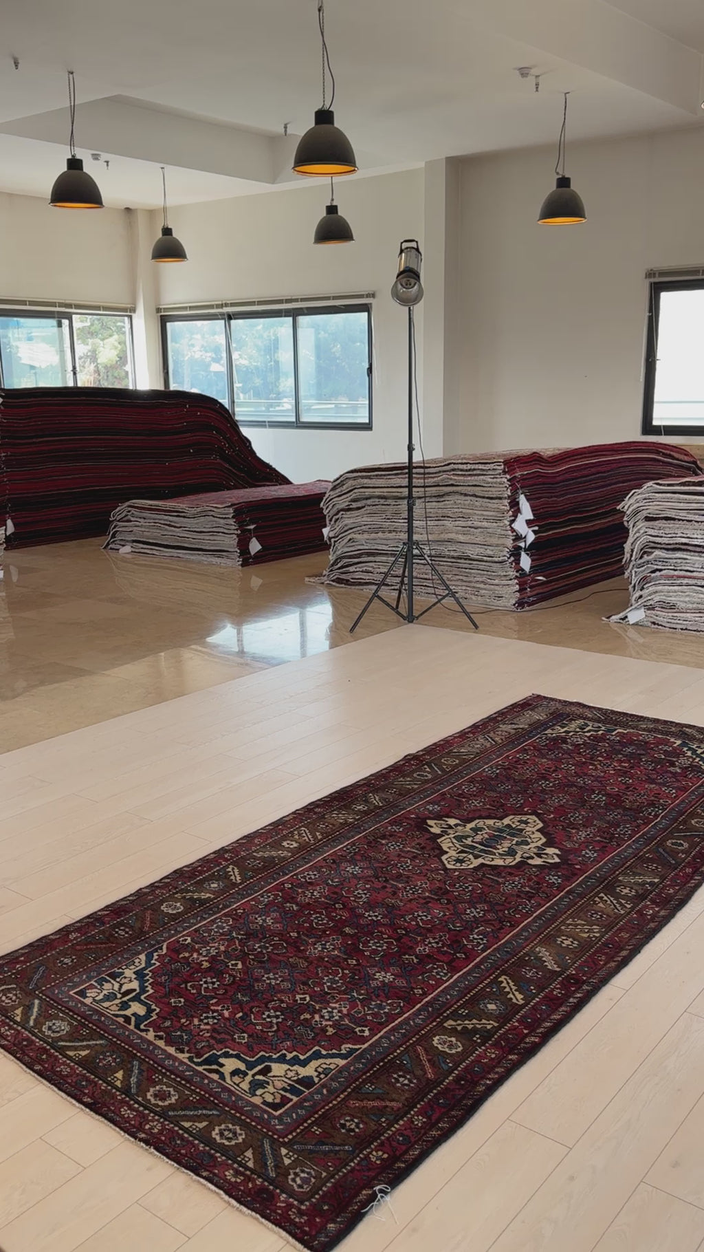 Vintage wool runner rug displayed in a showroom with stacked rugs, showcasing its rich red tones and traditional hand-knotted craftsmanship.