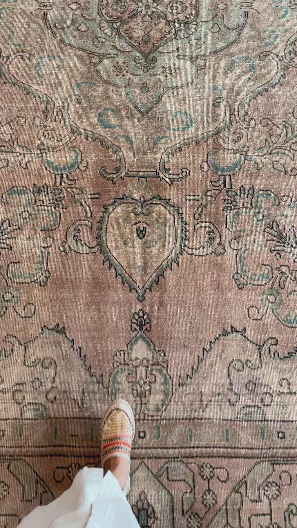 Close-up of hand-knotted vintage wool rug's faded floral pattern and texture, highlighting craftsmanship and soft pastel tones.
